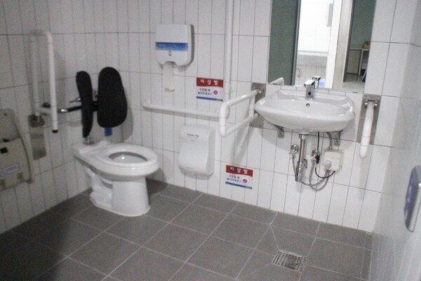 수원시 팔달문화센터 지하 1층 남녀장애인화장실 내부는 대변기에 자동 물 내림 센서와 등받이가 설치됐으며, 비상호출벨과 휴지걸이는 대변기에 앉았을 때 손이 닿는 곳에 위치해 있다. 세면대 양쪽 손잡이는 휠체어 접근을 용이 하게 하는 상하가동식인데, 세면대 밑에 배관 구조물이 있어 휠체어 접근을 방해한다. ©박종태