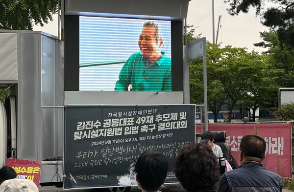 11일 국회 앞에서 열린 ‘전국탈시설장애인연대 김진수 공동대표 49재 추모제 및 탈시설지원법 입법 촉구 결의대회’에서 김진수 동지 추모영상을 시청하고 있다.ⓒ전국장애인차별철폐연대