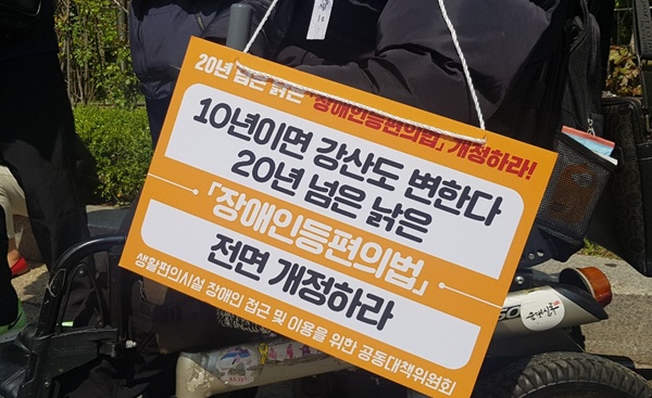 전동휠체어에 ‘10년이면 강산도 변한다. 20년 넘은 낡은 장애인등편의법 전면 개정하라’ 피켓이 걸려있는 모습. ⓒ에이블뉴스 DB
